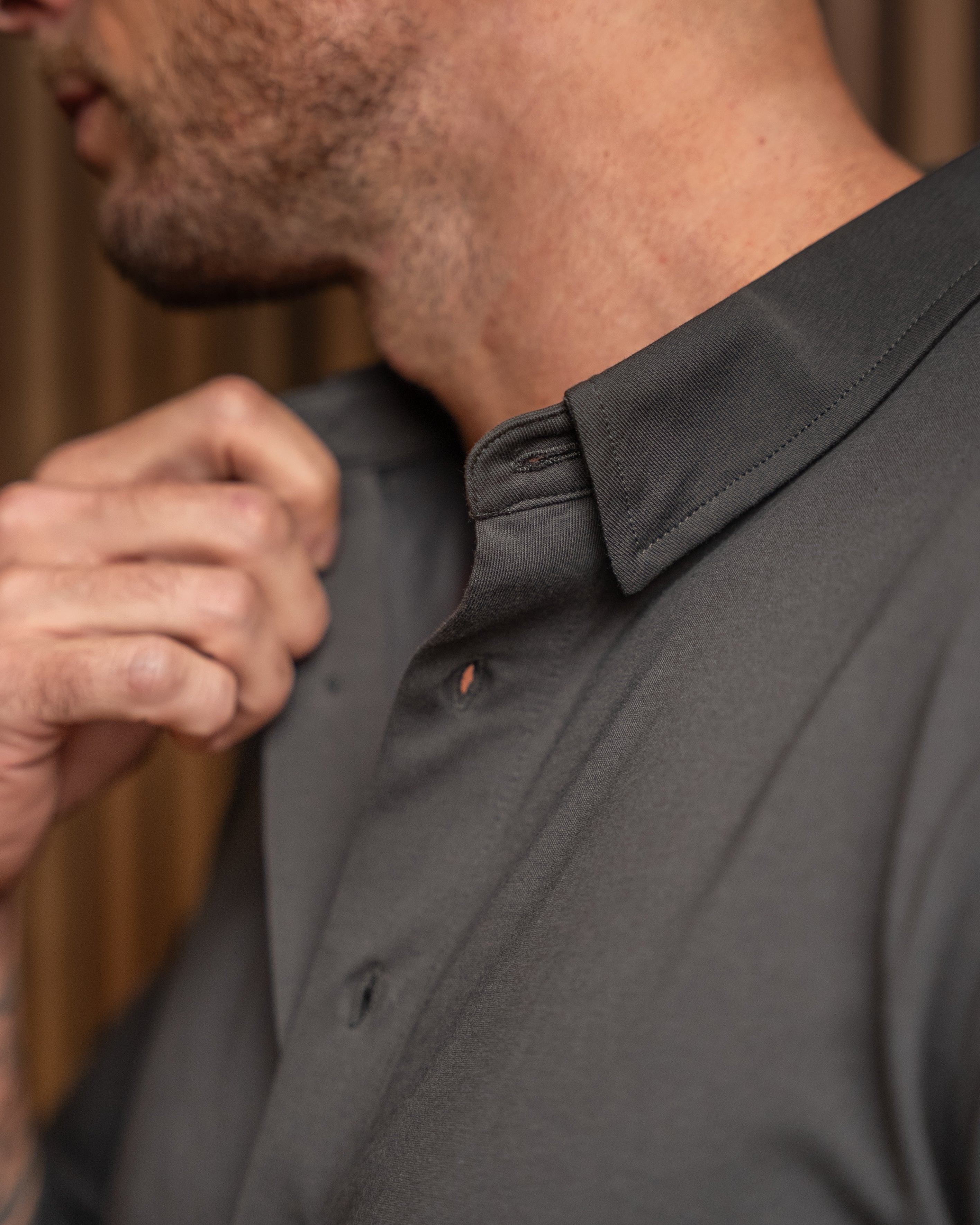 Close-up of a man wearing a dark charcoal gray button-down shirt, adjusting the collar with one hand.