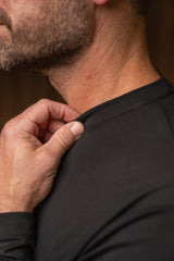 Close-up of a man's neck and shoulder wearing a black long-sleeve athletic shirt, with his hand pulling the collar slightly outward to show the fit.