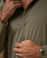 Close-up of a man wearing an olive green long-sleeve button-down shirt, adjusting the collar with one hand and buttoning the front with the other.