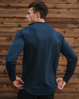 A man wearing a dark navy blue long-sleeve shirt, shown from the back against a rustic wooden plank wall.
