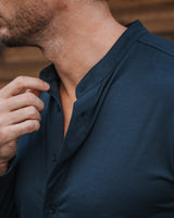 Close-up of a man wearing a dark navy blue button-up shirt with a mandarin collar, adjusting the collar with his hand.