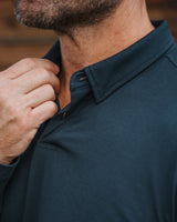 Close-up of a man wearing a dark teal polo shirt, adjusting the collar with one hand.