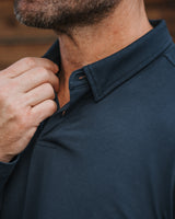 Close-up of a man wearing a dark teal polo shirt, adjusting the collar with one hand.