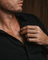 Close-up of a man wearing a black button-down shirt, adjusting the collar with one hand.