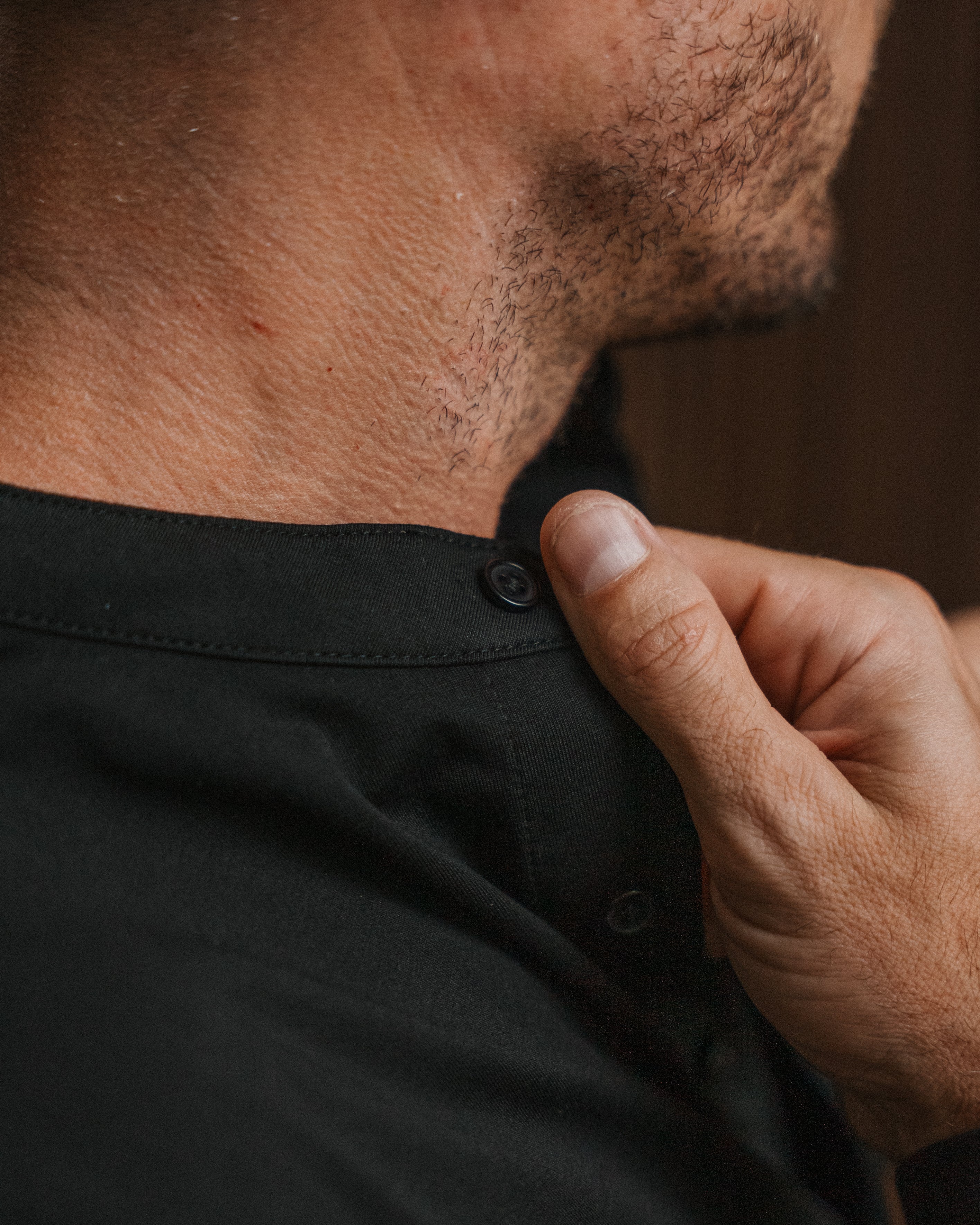 Close-up of a man wearing a black button-up shirt, adjusting the collar with his hand.