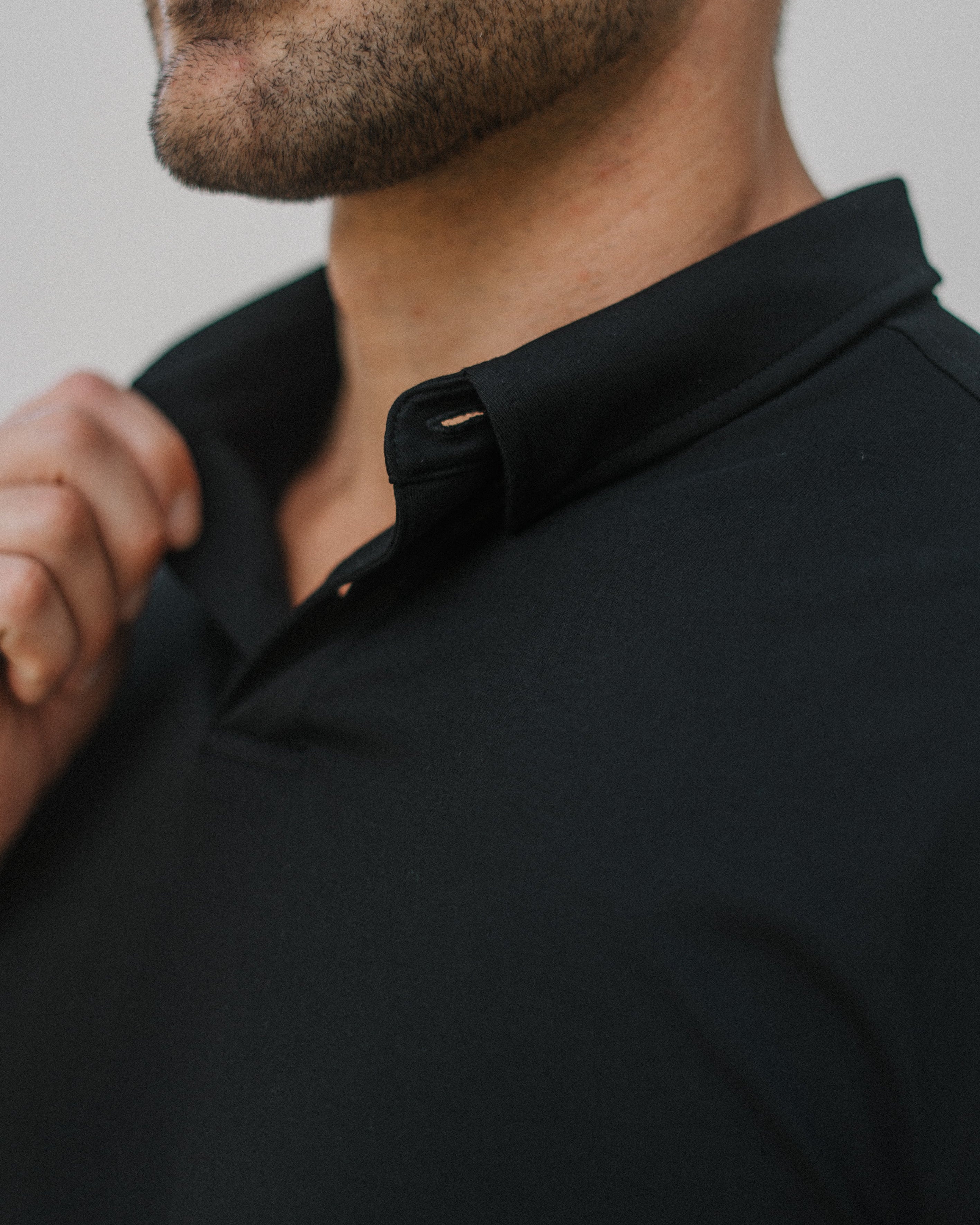 Close-up of a man wearing a black polo shirt, showing the collar and upper chest against a light gray background.