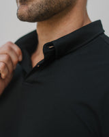 Close-up of a man wearing a black polo shirt, showing the collar and upper chest against a light gray background.