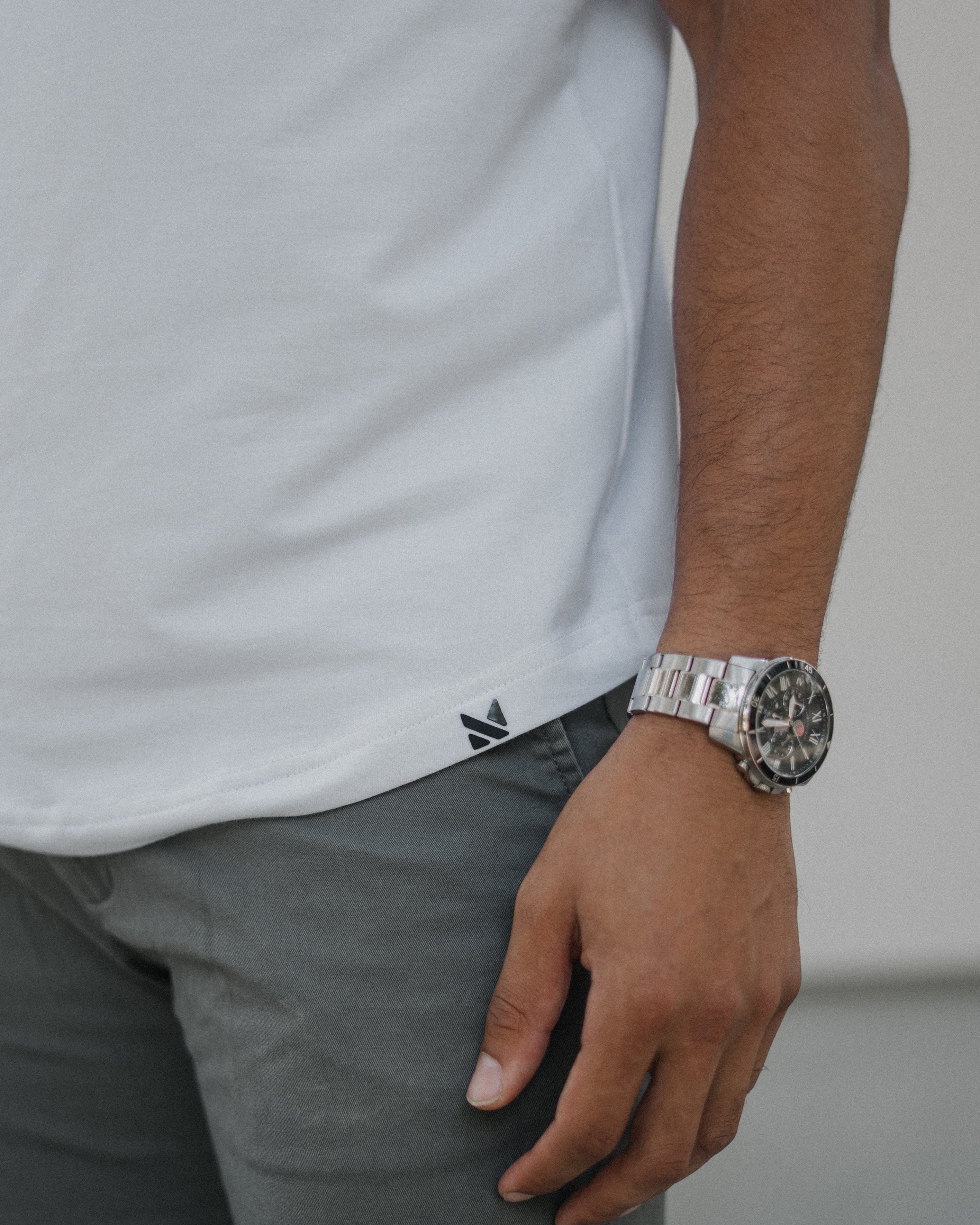 A close-up of a person wearing a silver metal link watch on their wrist, paired with a white t-shirt and gray trousers.