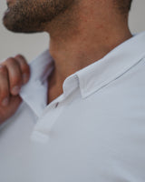 Close-up of a man wearing a white short-sleeve polo shirt, showing the collar, chest area, and part of his face and neck.