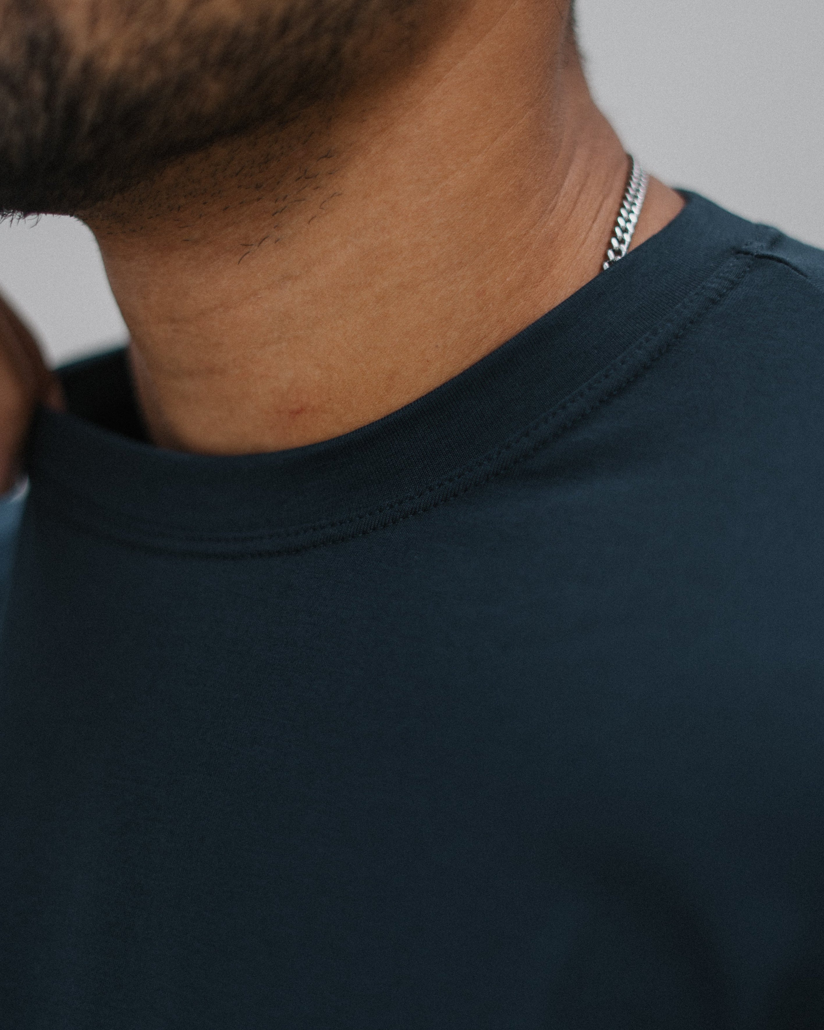 Close-up of a man wearing a dark navy crew-neck t-shirt and a silver chain necklace, showing the collarbone and neck area.