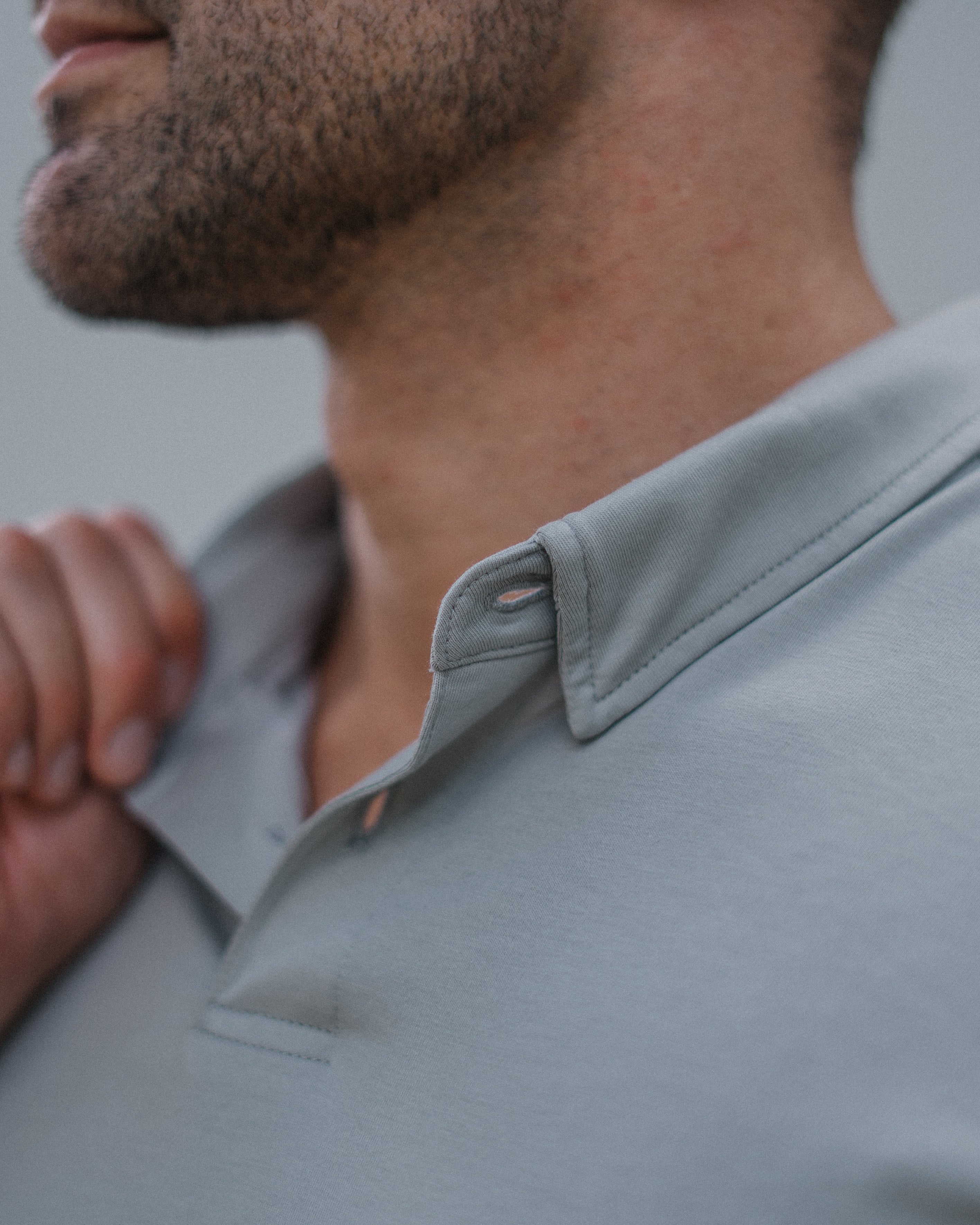 Close-up of a man wearing a light gray polo shirt, showing the collar, button, and fabric texture.