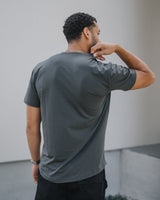 A man wearing a dark gray short-sleeve t-shirt, shown from behind as he looks over his shoulder in an outdoor setting.