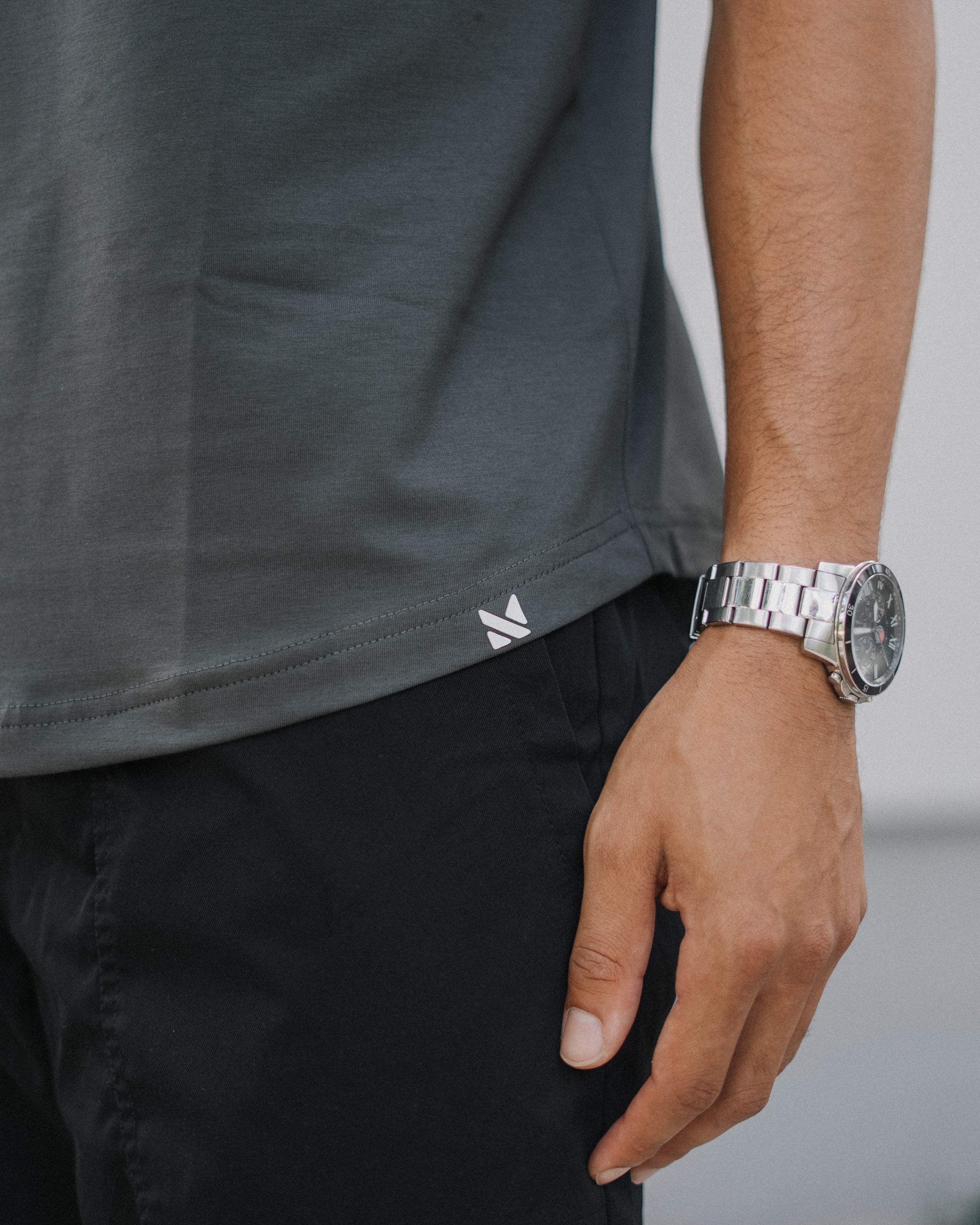 Close-up of a person wearing a dark gray short-sleeve athletic t-shirt and black cargo pants, with a silver metal link watch on the wrist.