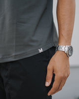 Close-up of a person wearing a dark gray short-sleeve athletic t-shirt and black cargo pants, with a silver metal link watch on the wrist.