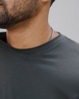 Close-up of a man's neck and lower face wearing a dark charcoal gray crewneck t-shirt and a silver chain necklace.