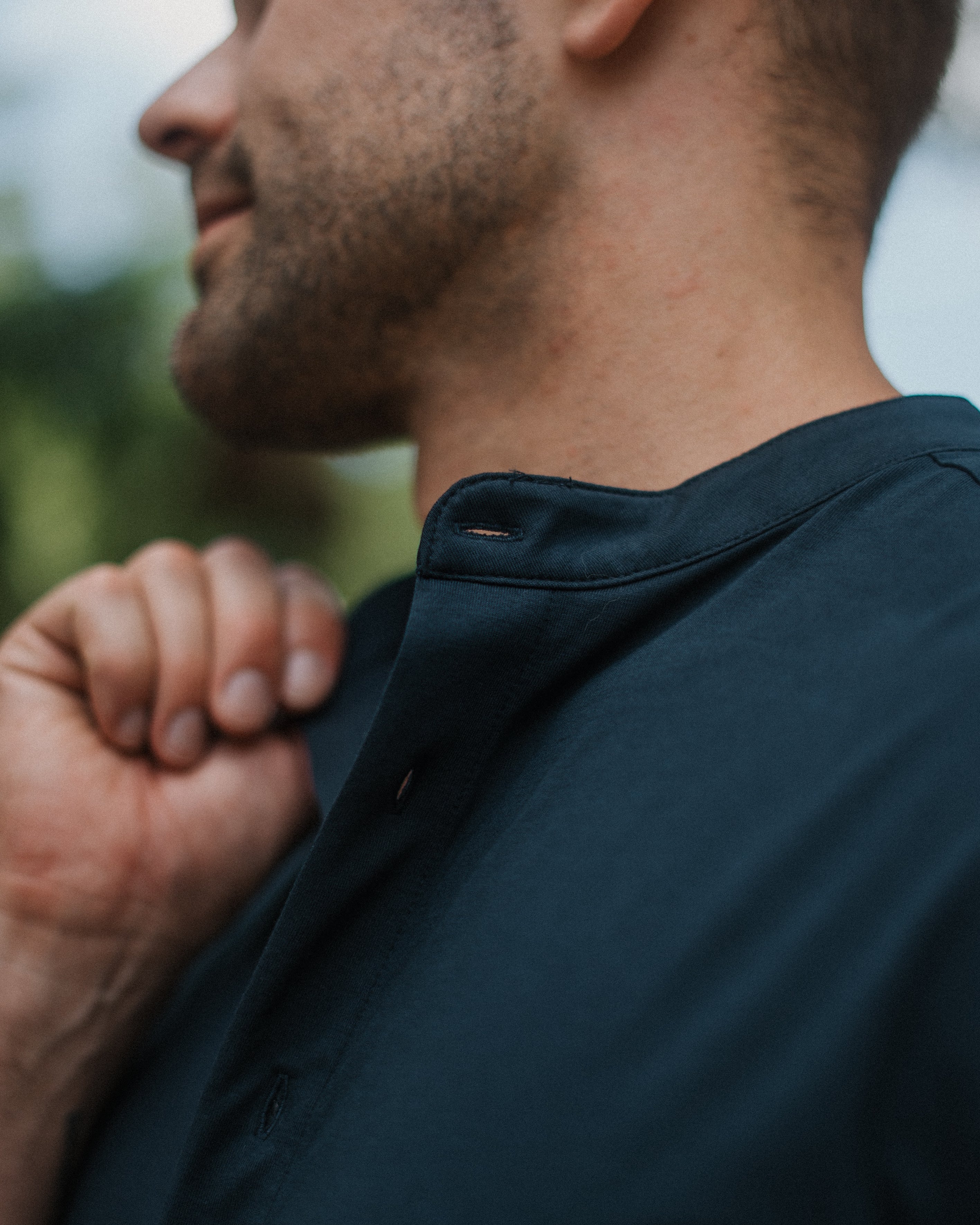 Close-up side profile of a man wearing a dark navy blue short-sleeve button-up shirt, showing the collar and fabric texture.