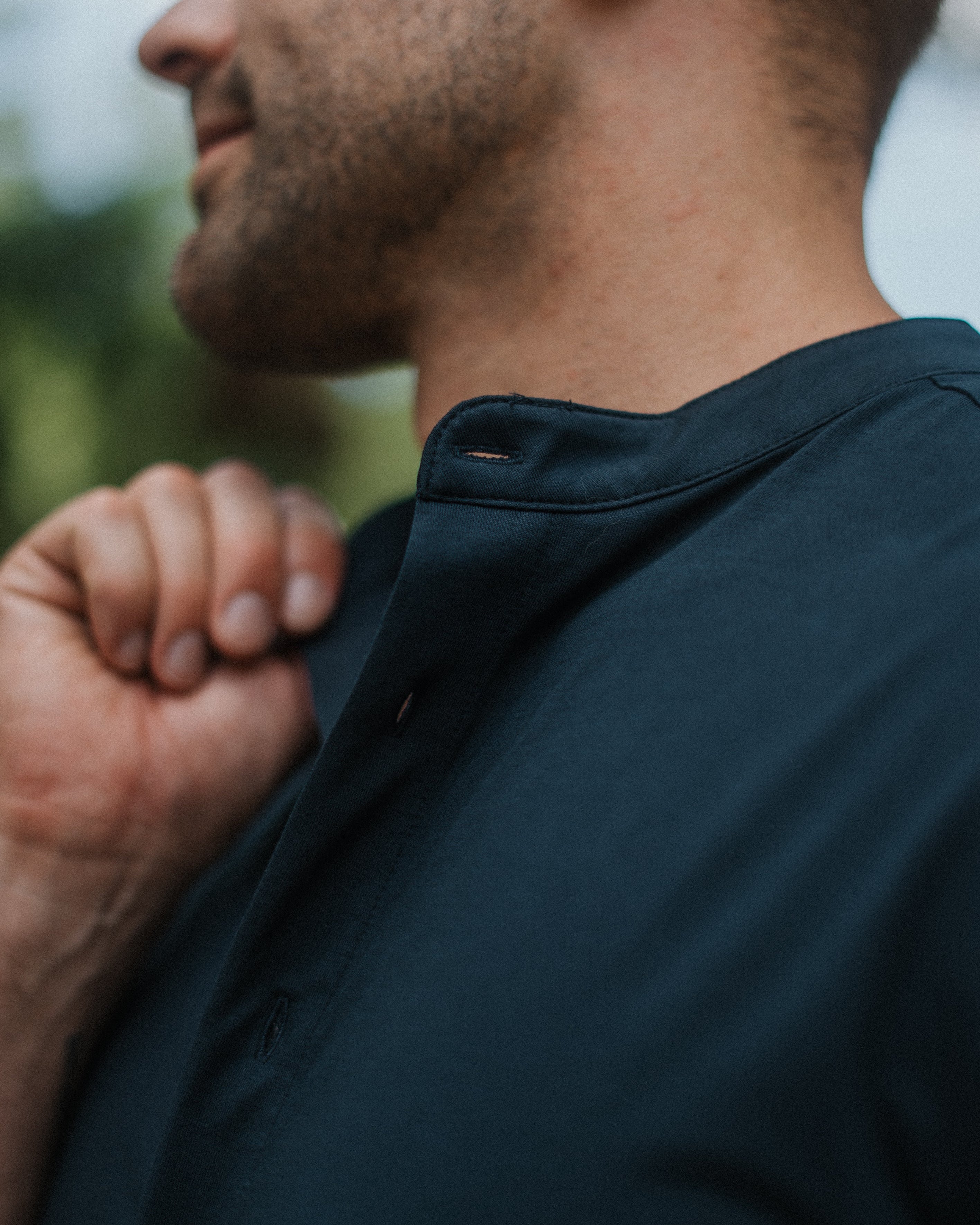 Close-up side profile of a man wearing a dark navy blue short-sleeve button-up shirt, showing the collar and fabric texture.
