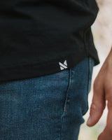 Close-up of a person wearing a black t-shirt and blue jeans, focusing on the side pocket area with a small white logo.