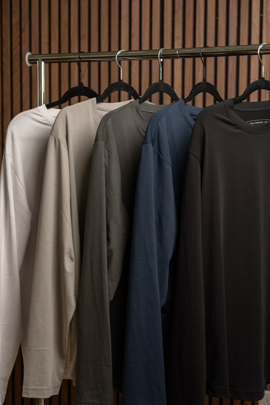 Noble Threads long-sleeve pieces hanging on a rack in cream, tan, olive, navy and black