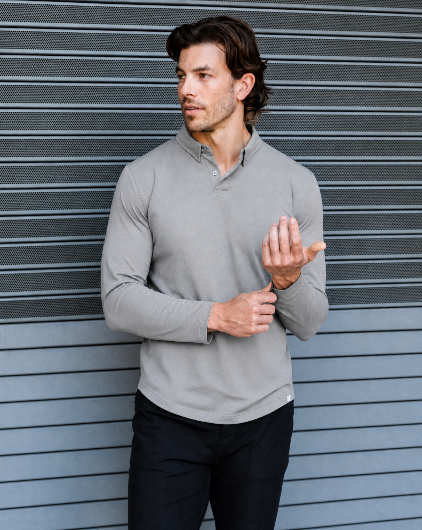 Man wearing a light gray long-sleeve shirt against a textured wall.