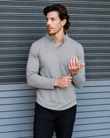 Man wearing a light gray long-sleeve shirt against a textured wall.